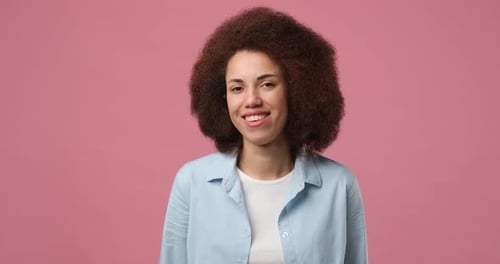 Smiling Attractive African American Woman Winks Looking at Camera Standing Over Pink Studio
