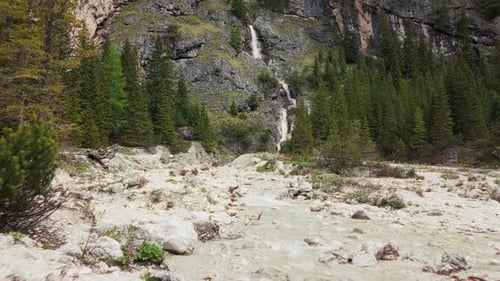 A mountain stream flows through rocky terrain with a cascading waterfall in the background, set in t