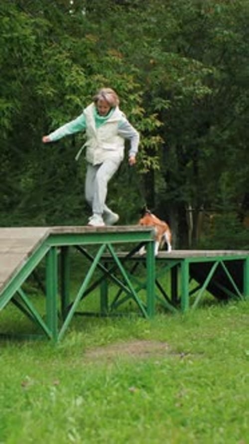 Woman Trains Dog on Agility Course Outdoors