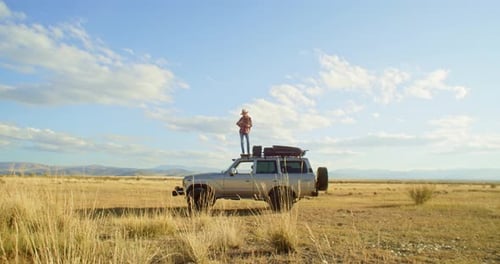 Traveler on SUV in a Field Under Sky