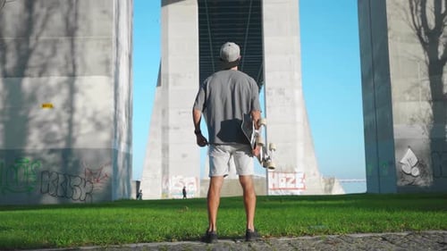 Man Holding Skateboard Under Bridge