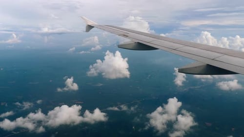 Airplane Wing View Above Clouds and Green Landscape