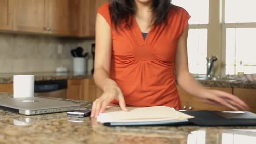 Woman Organizes Files and Laptop on Kitchen Counter