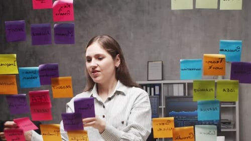 Young Business Woman is Doing Brainstorm Using Stickers on the Glass Office Worker is Thinking About