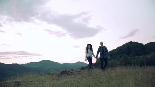 Couple Hiking Hand-in-Hand Across Mountain Meadow at Sunset