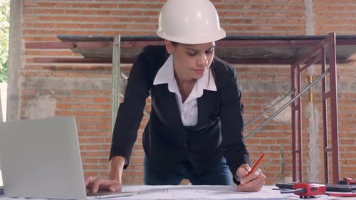Young caucasian architect woman looking laptop and working drawing blueprint.