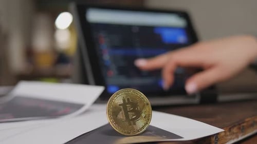 A Golden Bitcoin Coin a Woman Works with Graphs on a Cryptocurrency Exchange