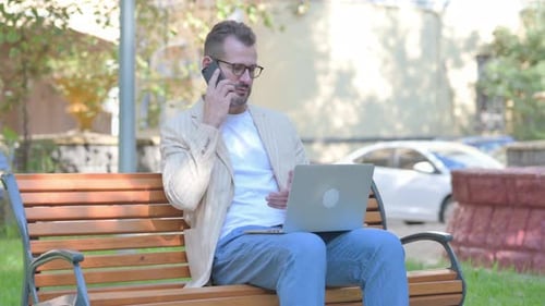 Man Working with Laptop and Phone on Bench