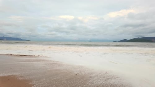 Cloudy Beach Scene with Waves Rolling Onto Shore at Sunset in a Coastal Location