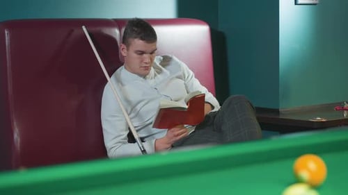 Young Man Reading Book Next to Pool Table