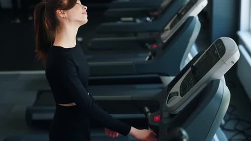 Walking and smiling. Woman in sportive clothes is running on the racetruck in the gym