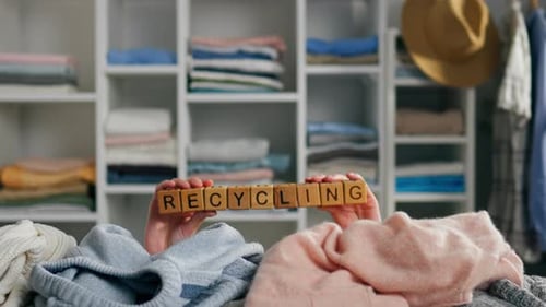 Hands Holding Blocks Spelling Recycling in Front of Clothes