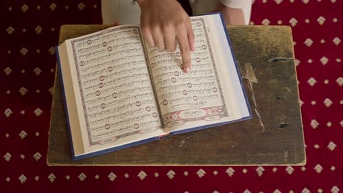 Nahaufnahme der Hände eines Muslims, der auf seinen Knien sitzt und in der Moschee mit dem Heiligen Koran betet