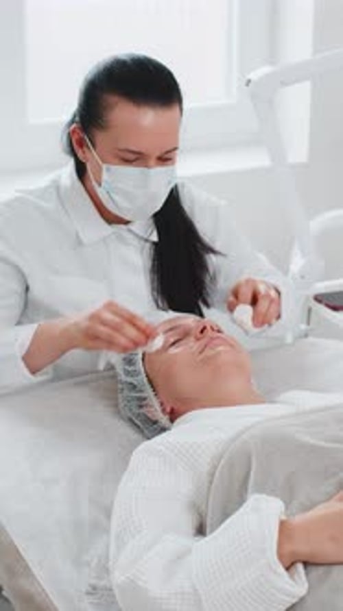 Cosmetologist Doctor Wipes Woman Face and Neck Cleaning Procedure with Cotton Wipes in Beauty Clinic