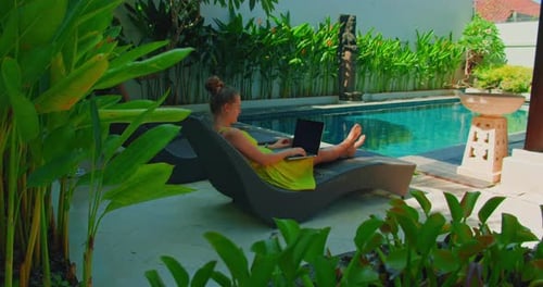 Freiberufliche Frau, die auf Laptop tippt, kommuniziert über das Internet in der Nähe eines Schwimmbads im Freien