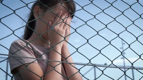 Sad Child Behind Chain Link Fence Covering Face
