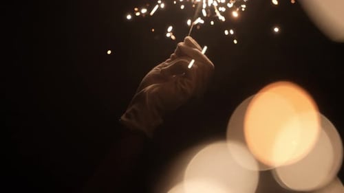Hand Holds Sparkling Sparkler Glowing in the Dark