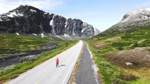 drone following young travel wearing red jacket jumping and celebrating life in a lovely road passin