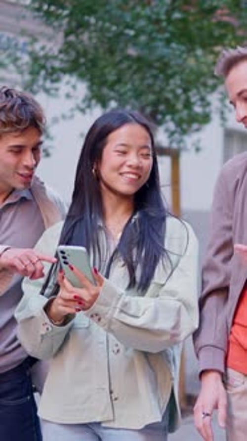 Friends Looking at Cellphone and Laughing on City Street