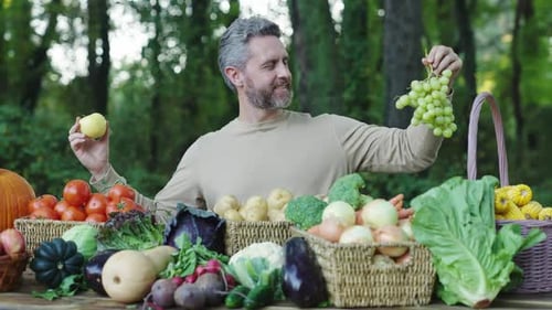 Man Holding Apple and Grapes at Outdoor Farmers Market Table Fresh Organic Vegetables and Fruits