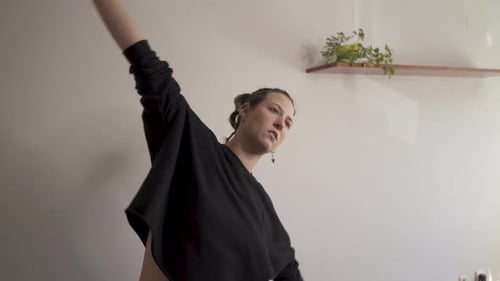 Altrenativa woman doing stretching at home with plants illuminated by window light