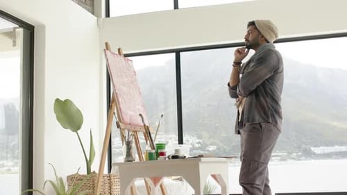 After placing brush by easel Indian artist surveying canvas planning strokes in studio, copy space