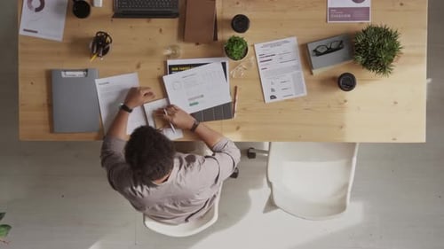 Ansicht von oben auf einen Büroangestellten, der Papierkram am Schreibtisch erledigt