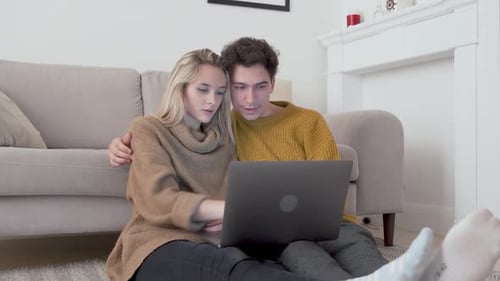 Couple using laptop sitting on floor at home