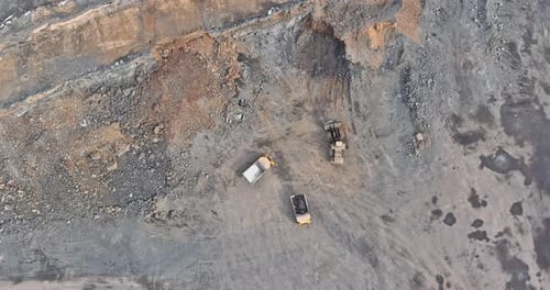 Bagger bei der Arbeit in einem Steinbruch, wobei beim Abbau von Kies Stein in einen Muldenkipper geladen wird