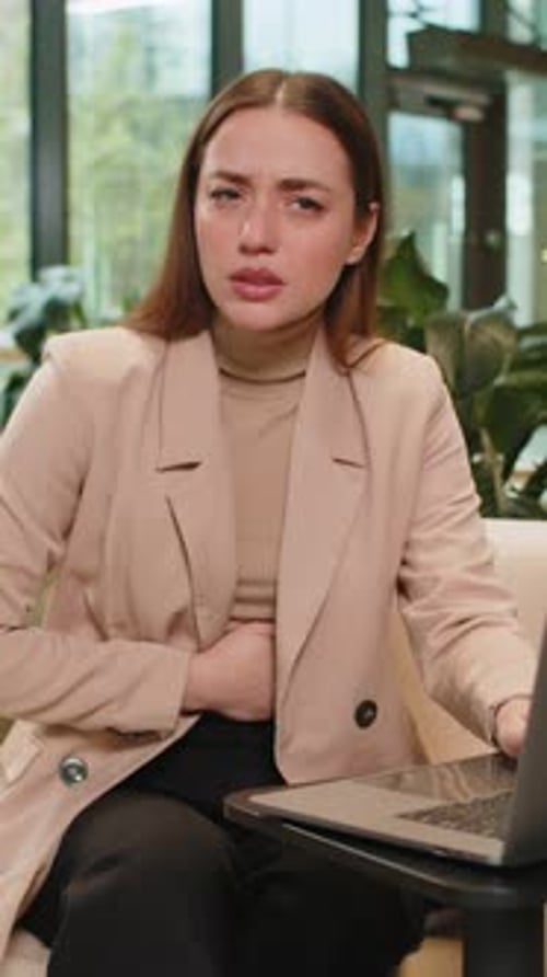 Disappointed Caucasian Businesswoman Using Laptop and Feeling Sudden Stomach Ache in Office Lobby