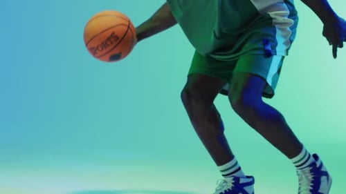 Video des Mittelteils eines afroamerikanischen männlichen Basketballspielers, der auf blauem Hintergrund einen Ball hüpft