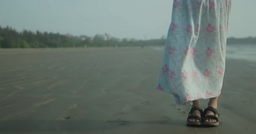 An indian woman legs is standing on a beach in India wearing a floral dress.
