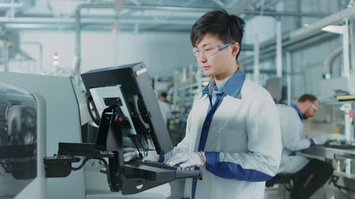 In einer High-Tech-Fabrik verwendet ein asiatischer Ingenieur einen Computer zur Programmierung von Elektronisch Pick-and-Place-Maschinen