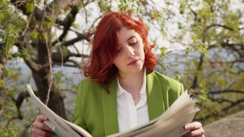 Geschäftsfrau mit roten Haaren liest Zeitung unter dem Baum