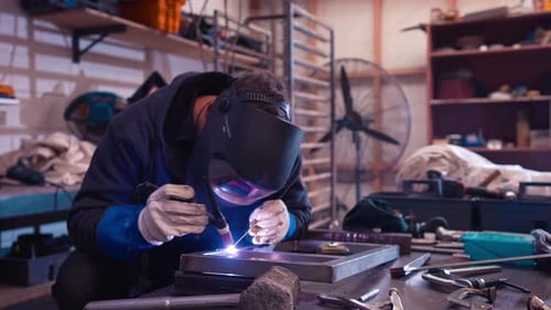 Welder using TIG welding machine to connect steel frame inside workshop