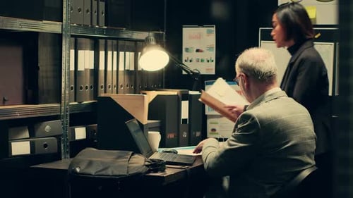 Colleagues Examine Documents Together in a Dim Office