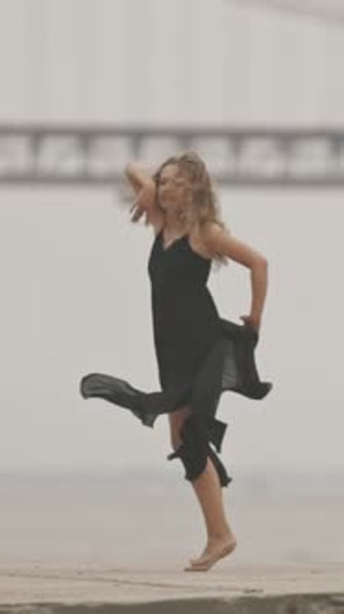 A Woman in Black Gracefully Dancing on the Pier in