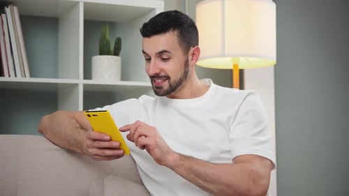 Smiling Young Adult Relaxing on Couch Using Smartphone