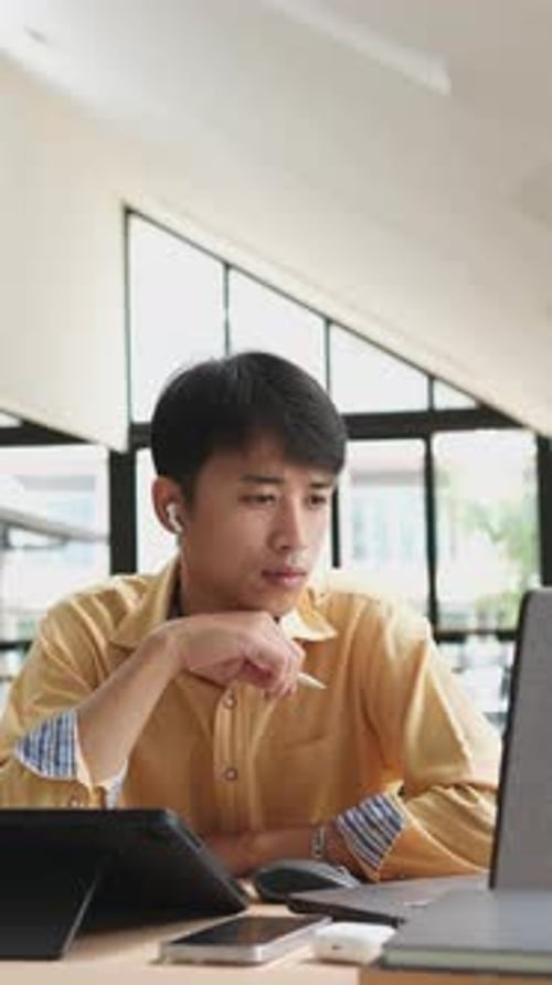 Ein Mann sitzt mit einem Laptop und einem Handy an einem Schreibtisch