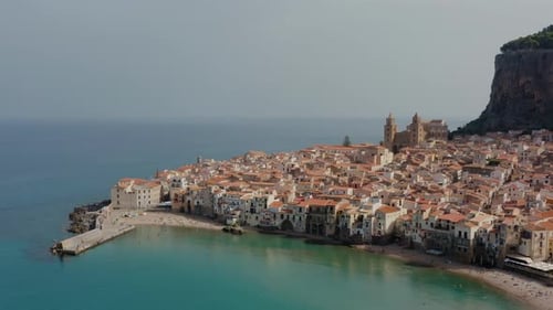 Descending aerial drone shot into the bay of Cefalu town. Sandy beach in a small historic town in Si