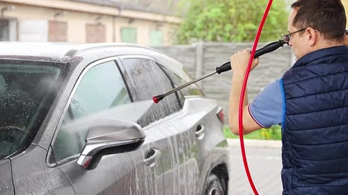 Young Man Washes His Car at a Selfservice Car Wash Using a Hose with Pressurized Water and Foam