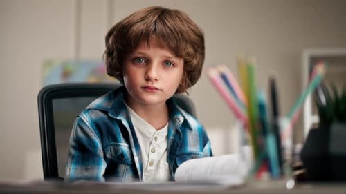 Nahaufnahme im Kinderzimmer ein Schuljunge in einem weißen Pullover und einem blau karierten Hemd an einem Schreibtisch