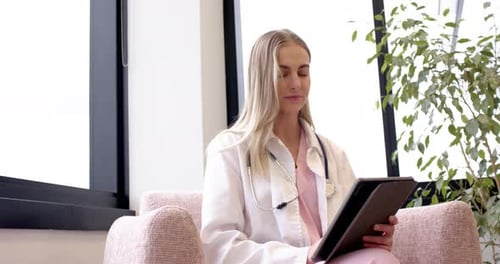 Frau im Laborkittel mit Stethoskop bereitet sich auf eine klinische Beratung vor, Notizen auf der Tablette mit Blick nach links