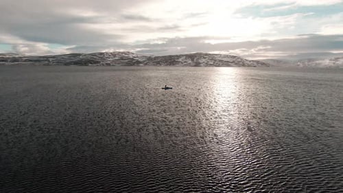 Man sitting on kayak in the middle of ocean, mountain scenery in background