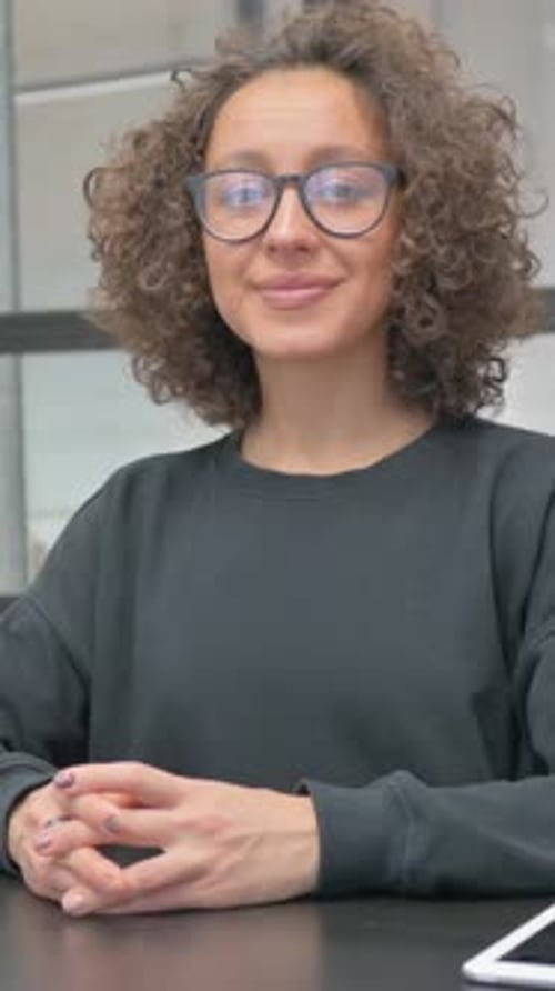 Woman Smiling with Curly Hair and Glasses Indoors