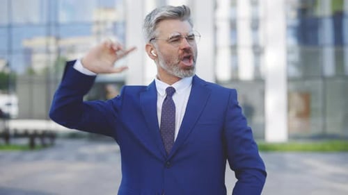 Glücklicher kaukasischer gutaussehender Geschäftsmann mit Brille und Kopfhörern feiert seinen Sieg