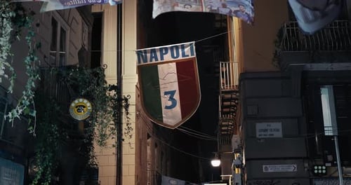 Napoli football crest displayed in city alley, night scene. Italy