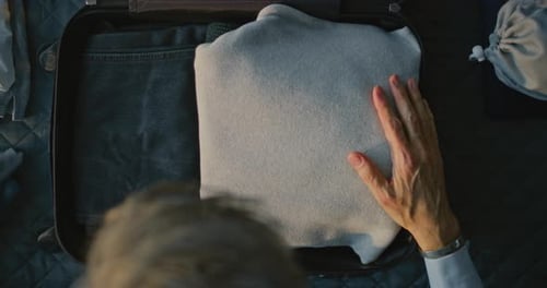 Mature Man Carefully Folding and Packing Clothes Into Suitcase on Neatly Made Hotel Bed