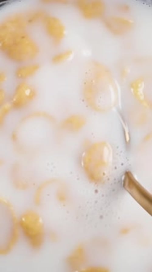 Plate of milk with wheat flakes, eat with a spoon. olly slider close up. Slow motion Vertical video.