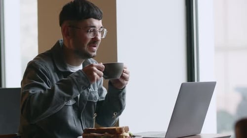 Freelancer Drinking Coffee While Working in Cafe Smiling Young Man in Glasses Using Laptop in
